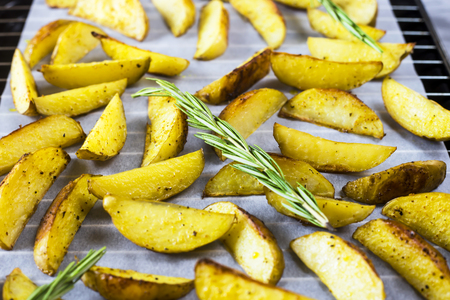 Baked potatoes on a baking sheet with pieces of spices and rosemary. Homemade cooking in the kitchenの写真素材