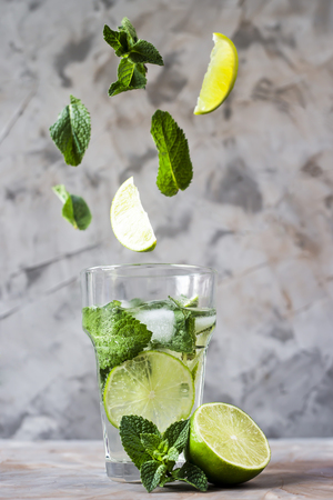 Leaves of mint and lime fly into a glass with mojito with ice on a gray background. Levitation flying magic items. Summer drinkの写真素材