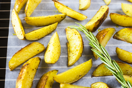 Baked potatoes on a baking sheet with pieces of spices and rosemary. Homemade cooking in the kitchenの写真素材