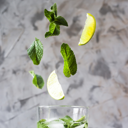 Leaves of mint and lime fly into a glass with mojito with ice on a gray background. Levitation flying magic items. Summer drinkの写真素材