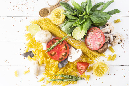 Food for cooking - pasta, basil, vegetables, lime and spices on a white wooden table in a heap. Top view, flat layの写真素材