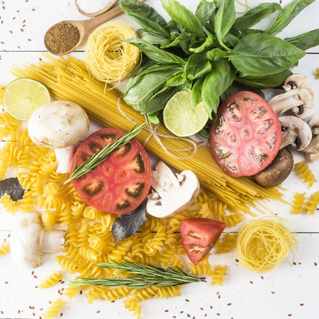 Food for cooking - pasta, basil, vegetables, lime and spices on a white wooden table in a heap. Top view, flat layの写真素材