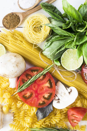 Food for cooking - pasta, basil, vegetables, lime and spices on a white wooden table in a heap. Top view, flat layの写真素材
