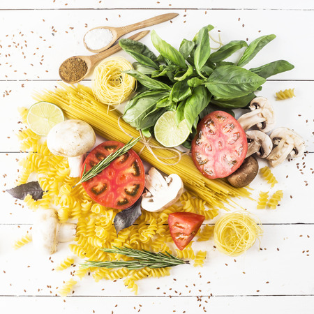 Food for cooking - pasta, basil, vegetables, lime and spices on a white wooden table in a heap. Top view, flat layの写真素材