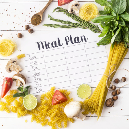 A meal plan for a week on a white table among products for cooking - pastas, basil, vegetables, lime, seeds, nuts and spices. Top view, flat lay, copyspaceの写真素材