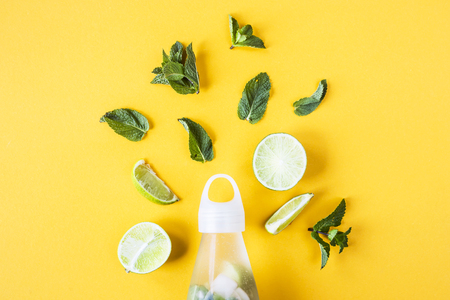 Ingredients for mojito lime and mint on a yellow background next to a transparent bottle with a refreshing summer drink. Top view, flat layの写真素材