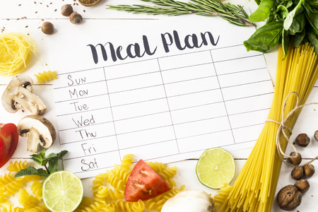 A meal plan for a week on a white table among products for cooking - pastas, basil, vegetables, lime, seeds, nuts and spices. Top view, flat lay, copyspaceの写真素材