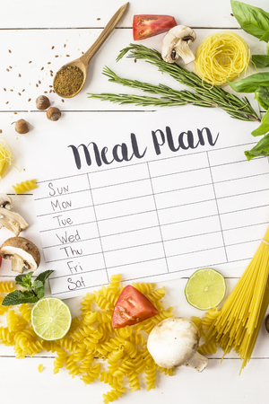 A meal plan for a week on a white table among products for cooking - pastas, basil, vegetables, lime, seeds, nuts and spices. Top view, flat lay, copyspaceの写真素材