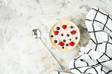 A bowl of oatmeal with raspberries and blueberries on a gray table next to a white checkered napkin. Healthy summer breakfast. Top view, flat lay, copyspaceの写真素材