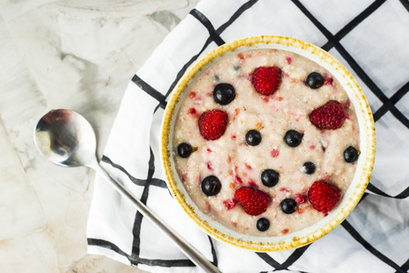 A bowl of oatmeal with raspberries and blueberries on a gray table next to a white checkered napkin. Healthy summer breakfast. Top view, flat layの写真素材