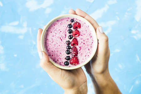 Berry smoothies with currants and raspberries in fwmalw hands on a bright blue background. Summer healthy snack. Top viewの写真素材