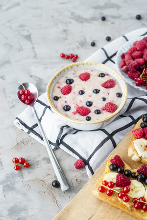 A table with a healthy summer breakfast - oatmeal with berries, currants and raspberries, and a sandwich with peanut butter, banana and various berriesの写真素材