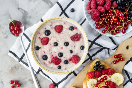 A table with a healthy summer breakfast - oatmeal with berries, currants and raspberries, and a sandwich with peanut butter, banana and various berries. Top view, flat layの写真素材