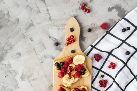 Sendvci with peanut butter, banana and raspberries and currants on a wooden board on a gray table. Vegan healthy breakfast. Top view, flat lay, copyspaceの写真素材