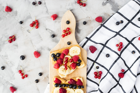 Sendvci with peanut butter, banana and raspberries and currants on a wooden board on a gray table. Vegan healthy breakfast. Top view, flat layの写真素材