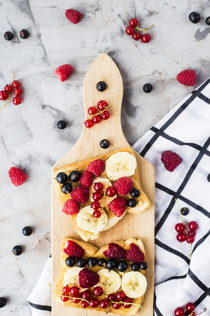 Sendvci with peanut butter, banana and raspberries and currants on a wooden board on a gray table. Vegan healthy breakfast. Top view, flat layの写真素材