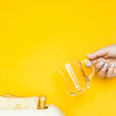 Toasted bread sticks out of the toaster on a yellow background. A woman's hand holds an empty cup for coffee. Breakfast conceptの写真素材