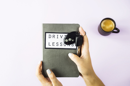 Female hands hold a training book for driving lessons and studying traffic rules and car keys. Getting a driving license concept. On a violet backgroundの写真素材