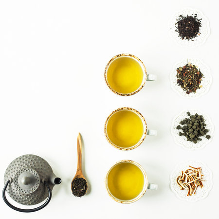 Cast iron kettle, cups with hot tea and dry tea lined with straight rows on a white background. Top...
