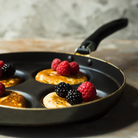 Red raspberries and black blackberries in a frying pan with round niches for pancakes. Summer pastry...