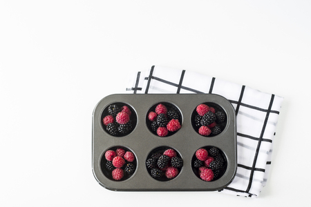 Raspberries and blackberries in the form for baking cupcakes on wight background. Summer cooking concept. Top view, flat layの写真素材