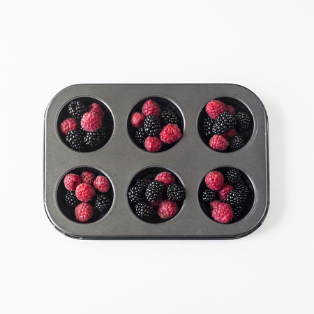 Raspberries and blackberries in the form for baking cupcakes on wight background. Summer cooking concept. Top view, flat layの写真素材