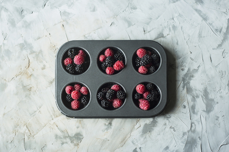 Raspberries and blackberries in metal form for cupcakes on a gray table. Summer baking concept. Top view, flat layの写真素材