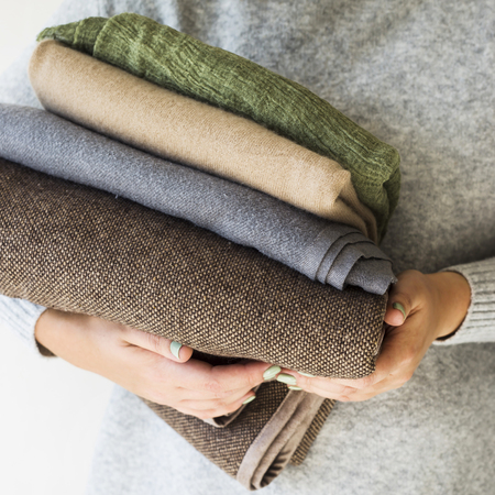 A stack of plaids and scarves in the hands of a woman in a gray sweater. Preparation in cold autumn and winter. Seasonal Wardrobe Conceptの写真素材