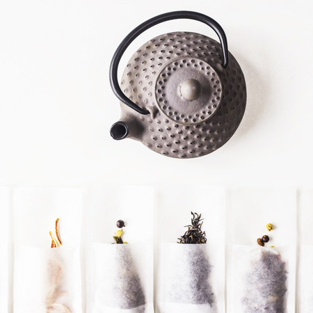 Different teas in a disposable filter bags for brewing next to a gray cast iron kettle on a white background. Top view, flat layの写真素材
