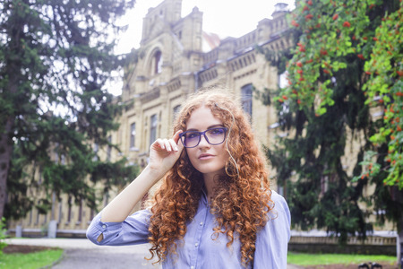Girl student with curly red hair in glasses for sight near the university building.の写真素材