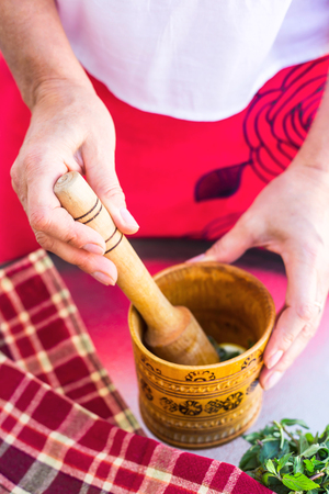 A woman holds a rustic wooden mortar in her hands and kneads peppermint for cooking or cospectology. Slow life Homemade conceptの写真素材