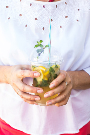 A woman in a white blouse holds a plastic glass with a mojito mug and a mint. Summer drink to cool outsideの写真素材