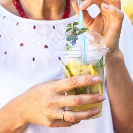 A woman in a white blouse holds a plastic glass with a mojito mug and a mint. Summer drink to cool...