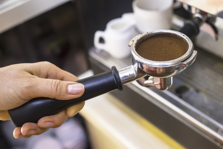 Holder from a coffee machine with ground coffee for espresso in the hands of a barista. Working with a coffee machine in a cafeの写真素材