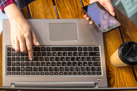 The girl is working behind a laptop at a table in a cafe next to a cup of coffee in a craft cup. Freelancer work concept. Top view, flat layの写真素材