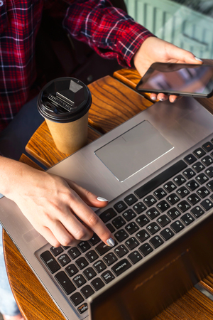 The girl is working behind a laptop at a table in a cafe next to a cup of coffee in a craft cup. Freelancer work concept. Top view, flat layの写真素材