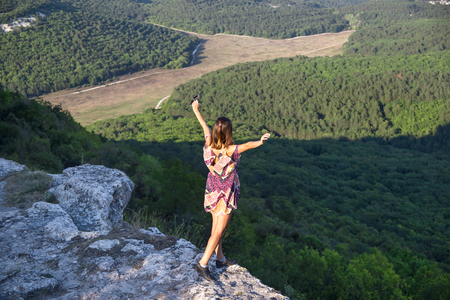 The girl is a traveler standing on top of a mountain and a cliff, stretching her arms forward. Active rest conceptの写真素材
