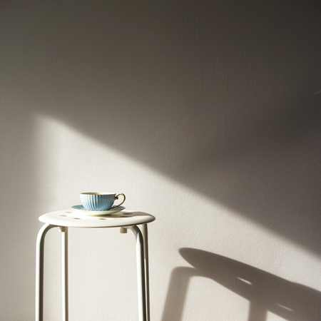 Blue vintage cup and saucer stands on a white stool against a white wall with shadow from the sun. Home cozy lifestyleの写真素材