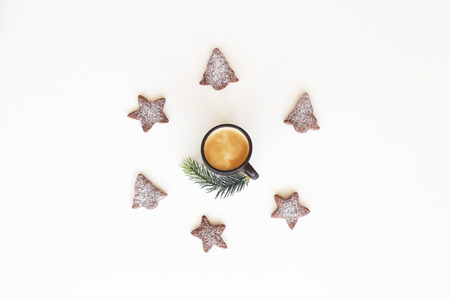Gingerbread cookies in the shape of a Christmas tree and stars with icing sugar are lined in a circle around a cup of coffee with a fir branch on a white background. Christmas and New Year in minimalism style Top view, flat layの写真素材