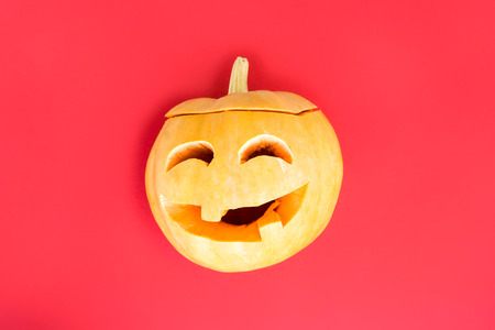 Pumpkin with carved eyes and mouth - decorations for Halloween on a red background. Minimalism. Top view, flat lay, copy spaceの写真素材