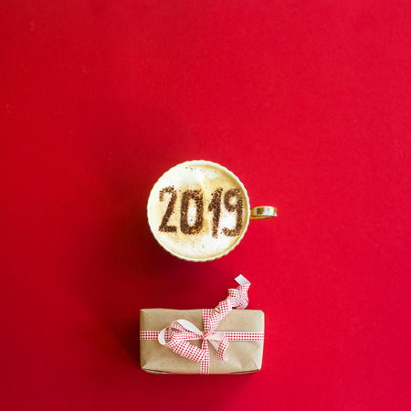 New Year 2019 is written on a cup of coffee with milk. The concept of the new year on January 1. On a red background with a gift. Top view, flat layの写真素材