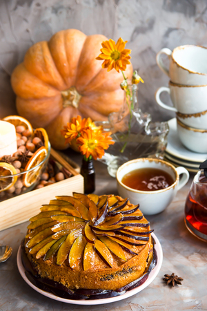 Plum cake decorated with sliced plum among the autumn decor - pumpkin, candle, oranges and yellow chrysanthemum. Rustic style. Homely cozy still lifeの写真素材