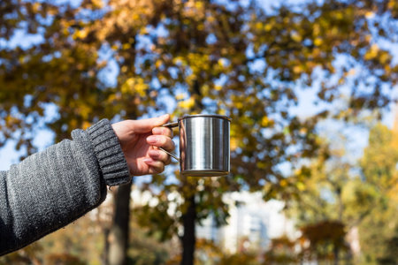 Metal cup with a hot drink in female hands. Knitted warm autumn clothes. Outdoor picnicの写真素材