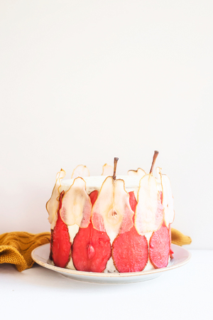 Festive white cake decorated with red and white pear slices On a white background among the gentle lights and candlesの写真素材