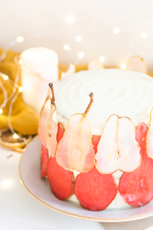 Festive white cake decorated with red and white pear slices On a white background among the gentle lights and candlesの写真素材