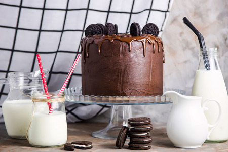 Chocolate cake with biscuits on a glass stand among the vessels with milk on a gray vintage background. Gourmet Pastry Conceptの写真素材