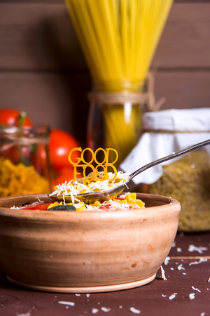 Good food is lined with pasta on a spoon near a plate with ready-made pasta with tomato, basil and parmesan on a wooden rural table. Healthy Vegan Nutrition Conceptの写真素材