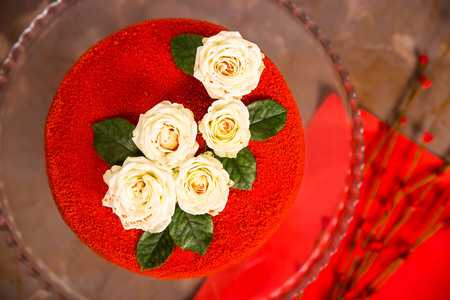 Red velvet cake decorated with white small roses with green leaves. Festive luxury cake for a birthday or weddingの写真素材