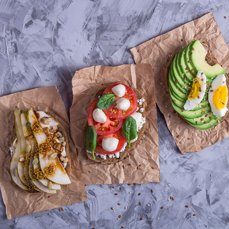 Beautiful healthy snack - sandwiches with rye bread with avocado and egg, mozzarella and tomato, cream cheese and pear. Healthy vegetarian food concept. Top view, flat layの写真素材