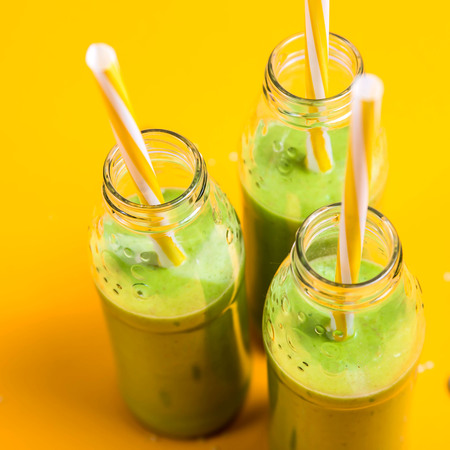 Green smoothies in three glass bottles with tubes on a bright yellow background. Healthy food detox concept. Copy spaceの写真素材